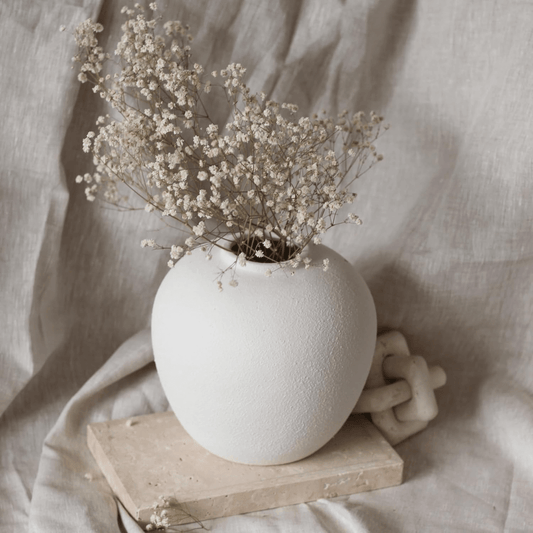 White textured vase with dried flowers on a wooden block against a soft beige fabric background