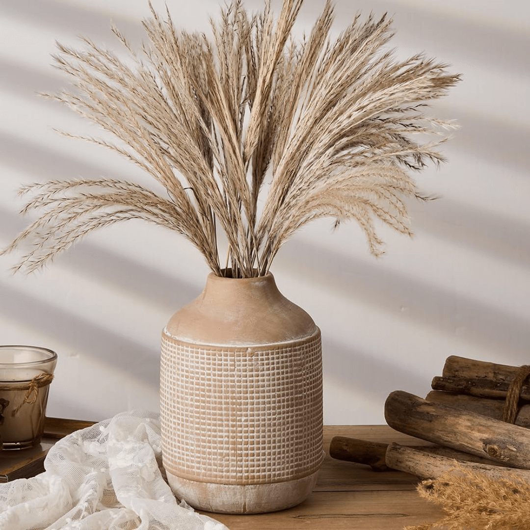 Decorative vase with dried grasses on a wooden surface with a neutral background