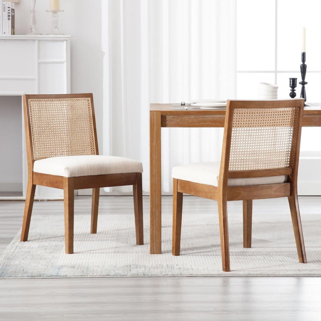 Two wooden chairs with wicker backrests and white cushions in a room with a table and decor.