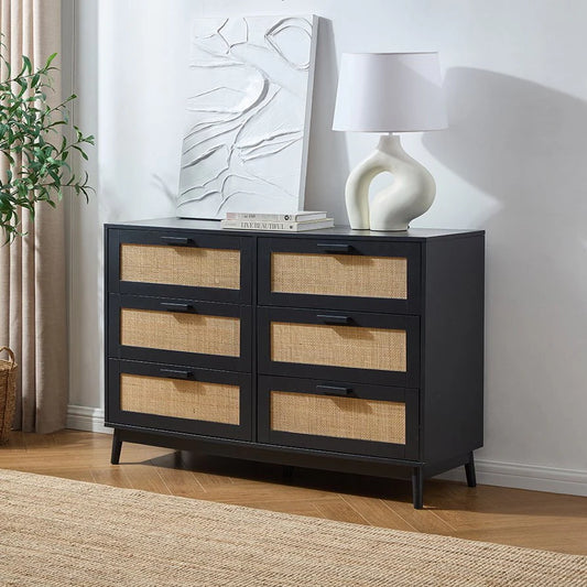 Black dresser with wicker drawers in a room setting with a lamp and plant.