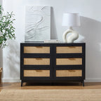 Black dresser with wicker drawers in a room with a lamp and abstract art on the wall.
