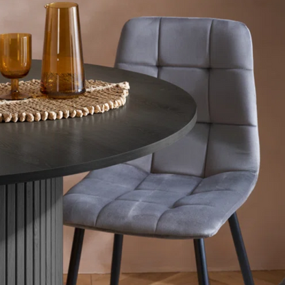 Gray upholstered chair next to a round dark table with decorative items.